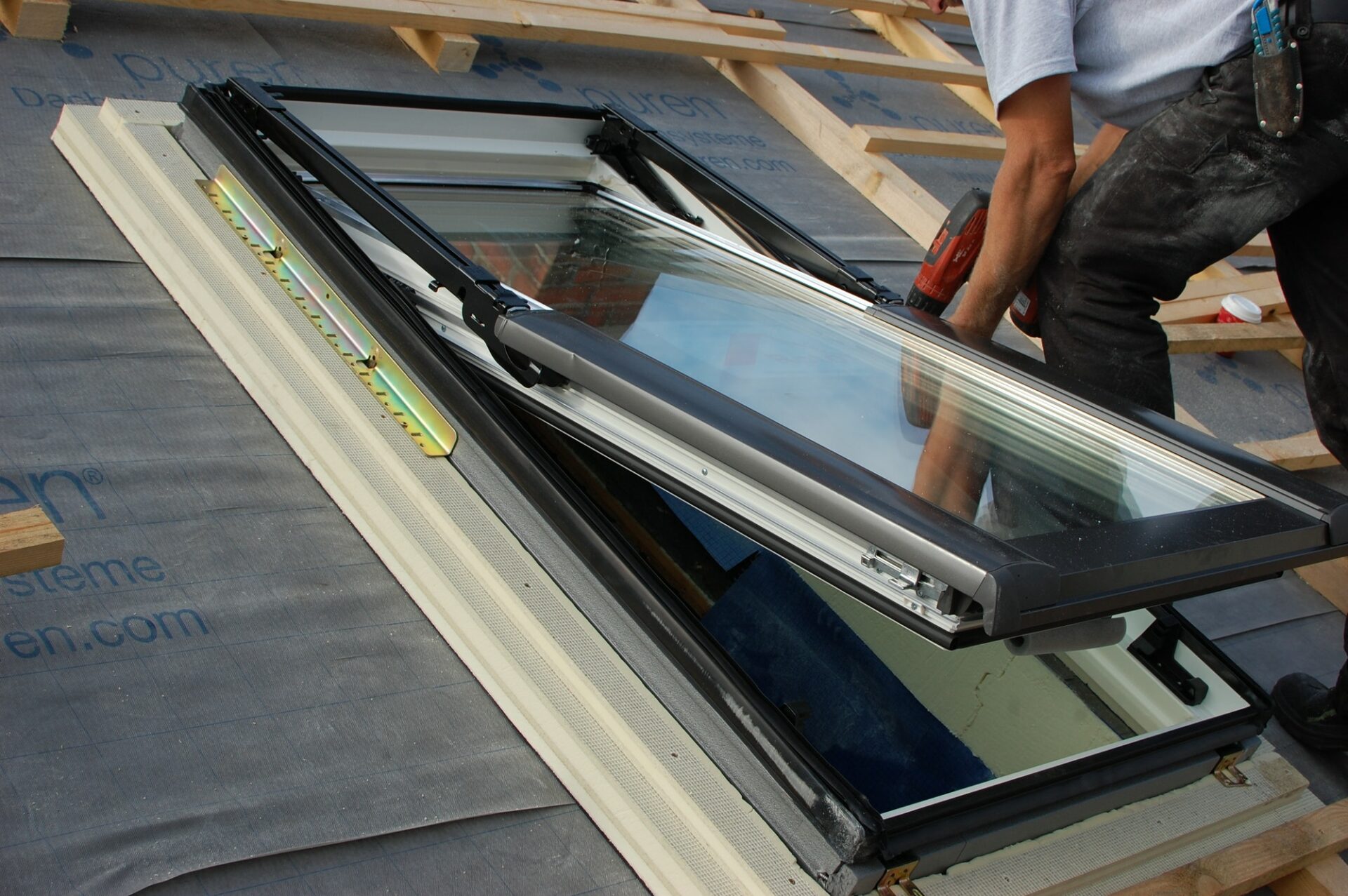 Assembling / fitting a roof window / skylight with reflection of worker in window glass