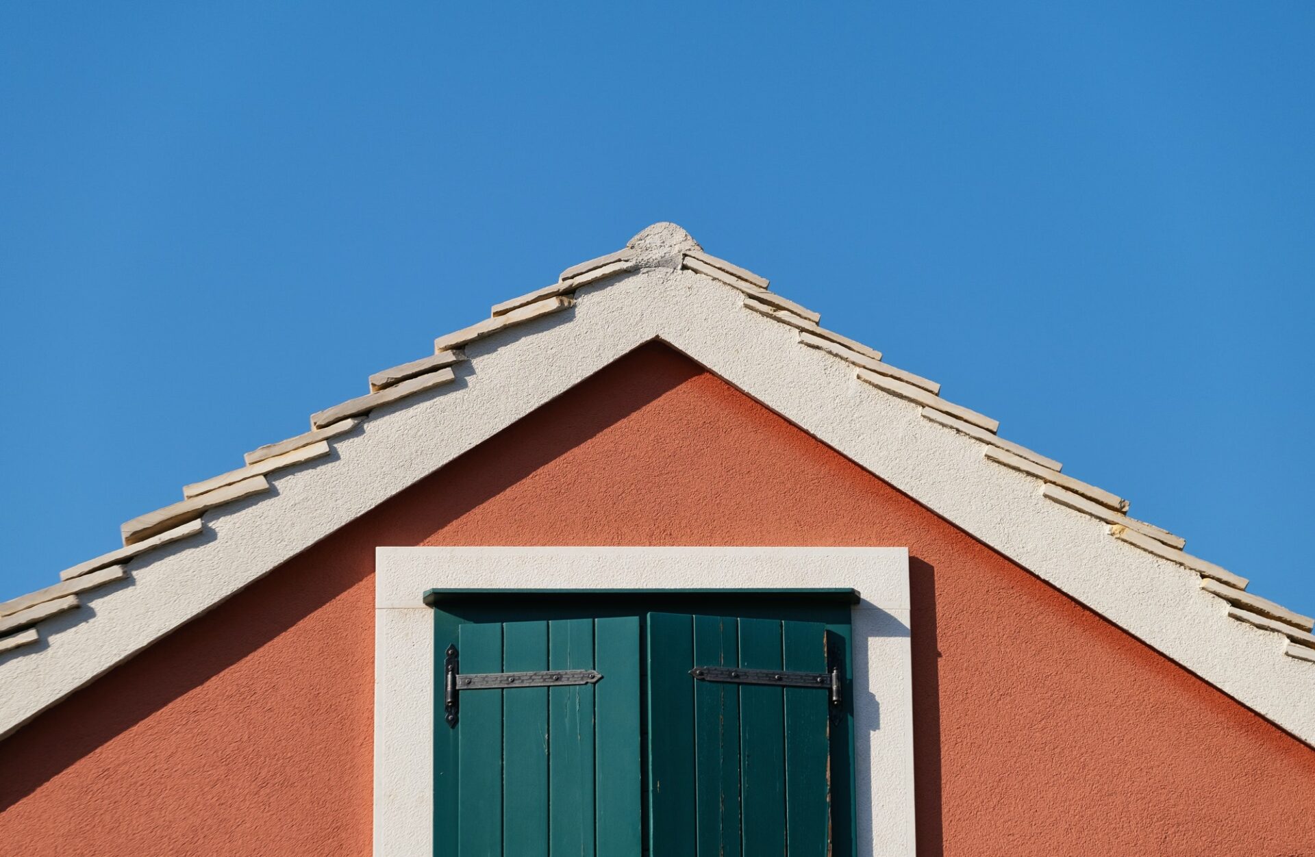 The house on the blue sky background. Roof and window with shutters.